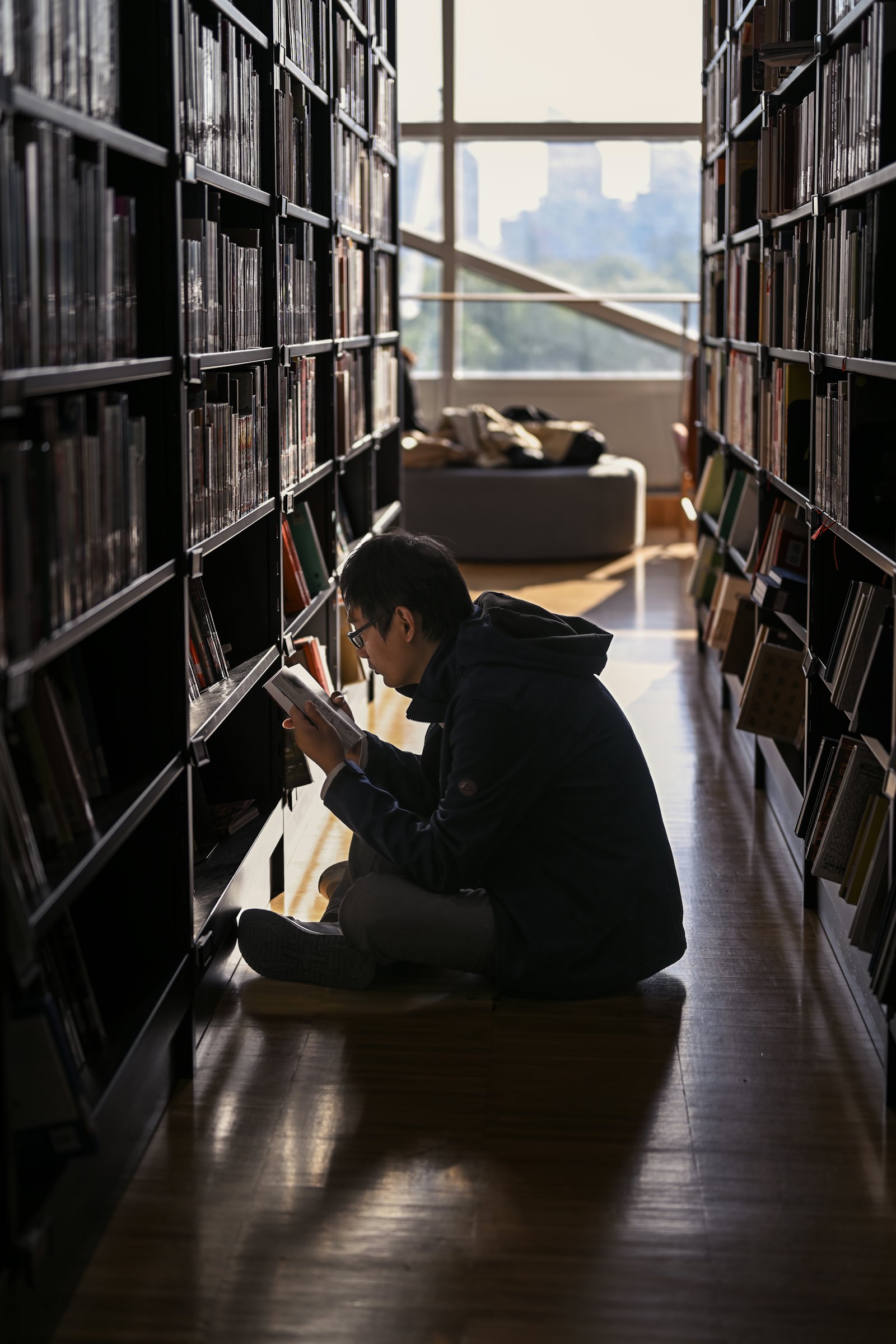 学生坐在图书馆书架旁认真阅读,光线透过窗户照入