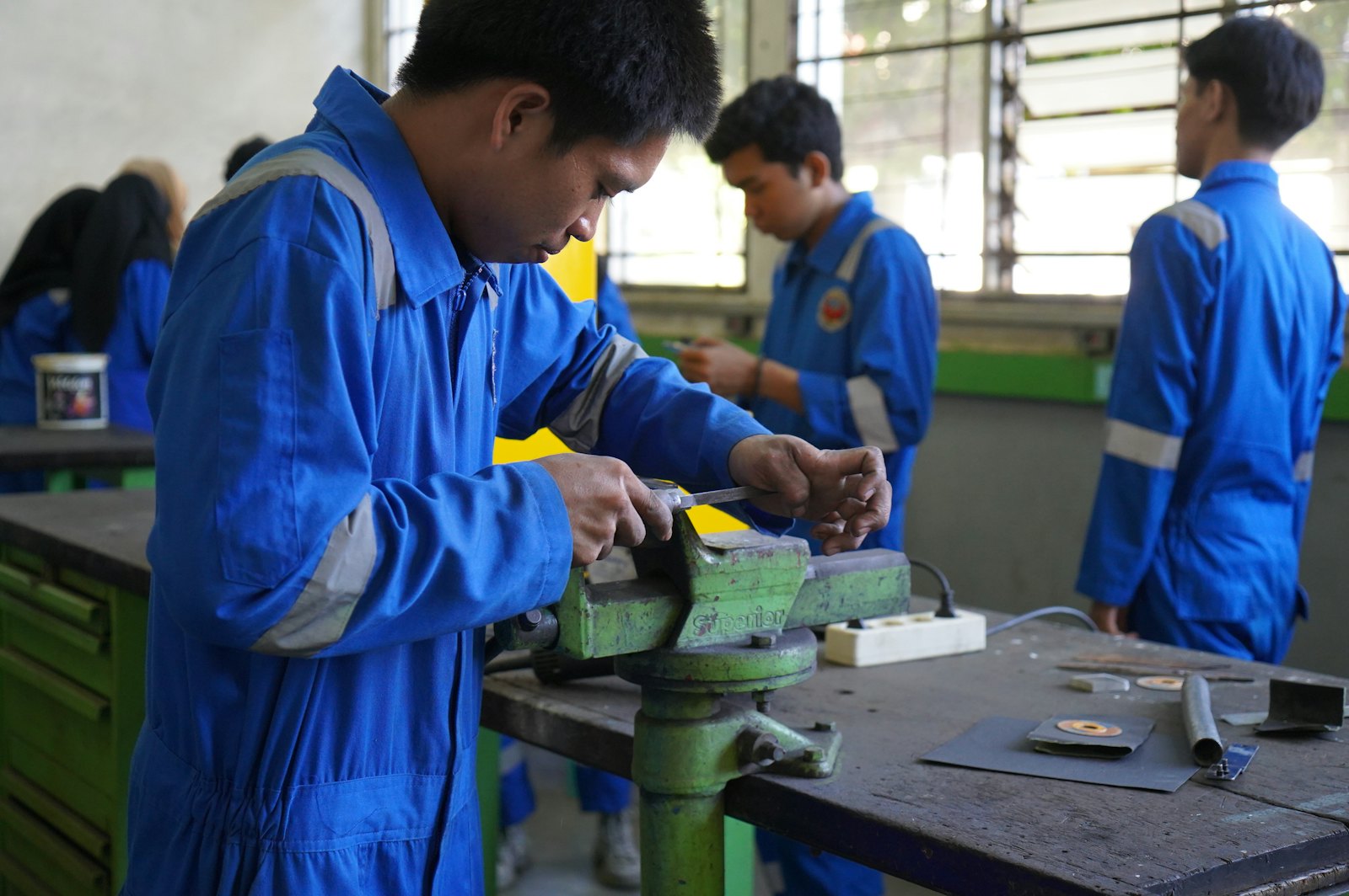 技工学院课堂实训场景，学生在动手操作金属加工工具