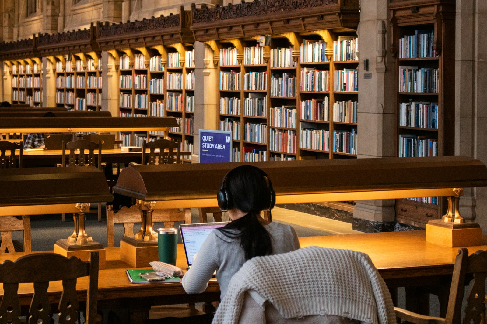 一名学生在图书馆安静自习区戴着耳机专注学习,书架前灯光温暖